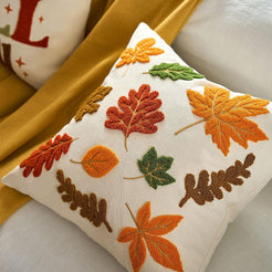 Embroidered polyester canvas pillow cover with raised autumn leaves in rust, orange and green, styled on a mustard throw