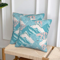 Set of two velvet pillow covers with aqua and blush mountains, styled on a woven chair