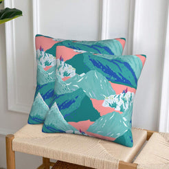 Set of two velvet pillow covers with teal mountains and coral sky, styled on a woven chair