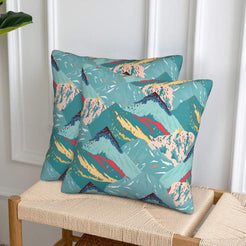Set of two velvet pillow covers with aqua mountains with coral accents, styled on a woven chair