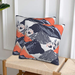 Set of two velvet pillow covers with charcoal mountains with coral accents, styled on a woven chair
