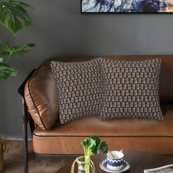 Velvet pillow covers with small brown block-print-inspired motifs, styled on a brown leather sofa