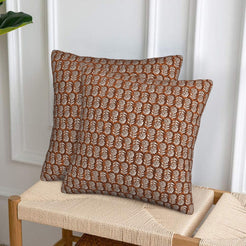 Velvet pillow covers with small rust block-print-inspired motifs, styled on a woven chair