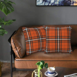 Fall velvet pillow covers with orange, black and white block plaid, styled on a brown leather sofa