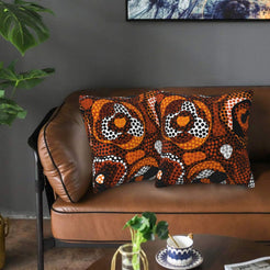 Velvet pillow covers with orange and brown circular dot motifs, styled on a leather sofa