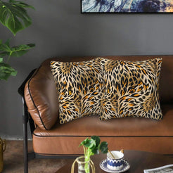 Velvet pillow covers with swirling tiger and leopard markings, styled on a brown leather sofa