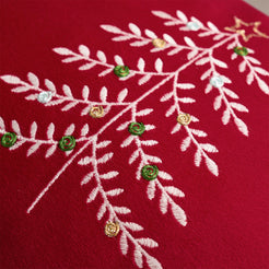 Close-up of embroidered Christmas tree branches on red velvet