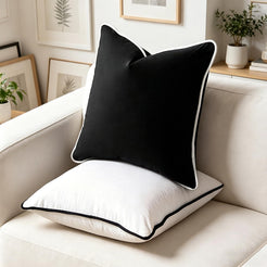 Velvet pillow covers with black velvet with white piping, stacked on a cream chair