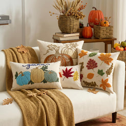 Embroidered polyester canvas pillow covers with autumn leaf and pumpkin designs, grouped on a cream sofa