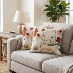 Embroidered polyester canvas pillow covers with rust, cream and green embroidered wildflowers, styled on a gray sofa