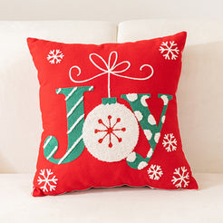embroidered polyester canvas pillow cover with JOY lettering, ornament and snowflakes on red, shown on a cream sofa