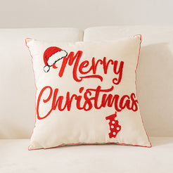 embroidered polyester canvas pillow cover with Merry Christmas lettering and Santa hat on cream, shown on a cream sofa