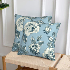 Set of two velvet pillow covers with light blue rose print, styled on a woven chair