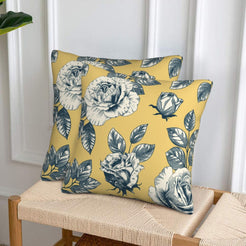Set of two velvet pillow covers with mustard yellow rose print, styled on a woven chair