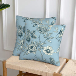 Set of two velvet pillow covers with light blue floral branches, styled on a woven chair