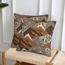 Set of two velvet pillow covers with brown and tan mountains, styled on a woven chair