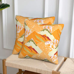 Set of two velvet pillow covers with orange and cream mountains, styled on a woven chair
