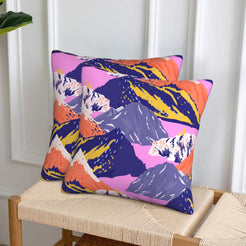 Set of two velvet pillow covers with navy mountains with pink and coral accents, styled on a woven chair
