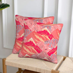 Set of two velvet pillow covers with coral and pink mountains, styled on a woven chair