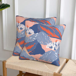 Set of two velvet pillow covers with slate blue mountains with coral accents, styled on a woven chair