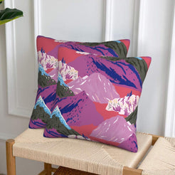 Set of two velvet pillow covers with magenta, purple and teal mountains, styled on a woven chair