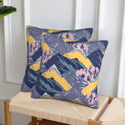 Set of two velvet pillow covers with charcoal mountains with yellow and lilac accents, styled on a woven chair