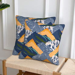 Set of two velvet pillow covers with navy mountains with orange and yellow accents, styled on a woven chair