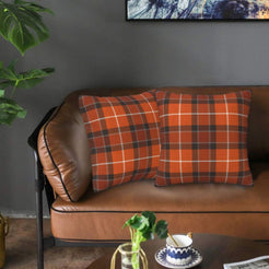 Fall velvet pillow covers with orange and white windowpane plaid, styled on a brown leather sofa