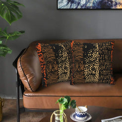Velvet pillow covers with black and orange African-inspired symbols, styled on a leather sofa