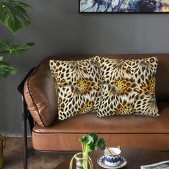 Velvet pillow covers with pale leopard rosettes and gray feathered streaks, styled on a brown leather sofa