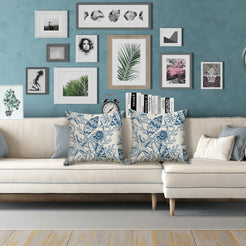 Water-resistant linen-look polyester pillow covers with blue conch shells and coral, styled on a cream sofa