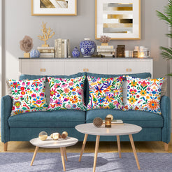 Short-pile plush pillow covers with bright Mexican-inspired floral patterns on white, styled on a teal sofa