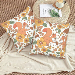 Set of two velvet pillow covers with cream squirrel, acorn and floral pattern, styled on a woven chair