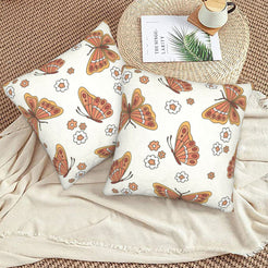 Set of two velvet pillow covers with cream butterflies and small flowers, styled on a woven chair