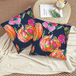 Set of two velvet pillow covers with navy pumpkins and vivid pink flowers, styled on a woven chair