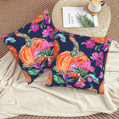 Set of two velvet pillow covers with navy pumpkin and pink floral pattern, styled on a woven chair