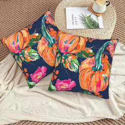Set of two velvet pillow covers with navy pumpkins and pink roses, styled on a woven chair