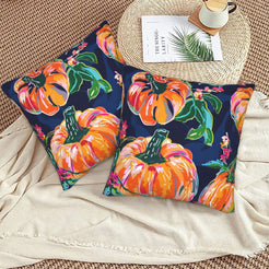 Set of two velvet pillow covers with navy pumpkins and autumn leaves, styled on a woven chair