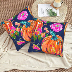 Set of two velvet pillow covers with navy pumpkin and pink rose pattern, styled on a woven chair