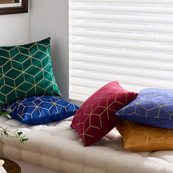 Embroidered velvet pillow covers with burgundy, blue and emerald geometric designs, arranged on a cream sofa