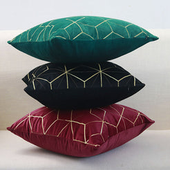 Embroidered velvet pillow covers with emerald, black and burgundy geometric designs, stacked on a sofa