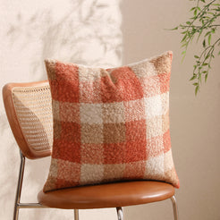 Bouclé-textured polyester pillow cover with rust orange, cream and taupe plaid, styled on a chair