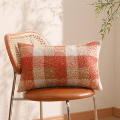 Bouclé-textured polyester pillow cover with rust orange, cream and taupe plaid, shown in lumbar size on a chair