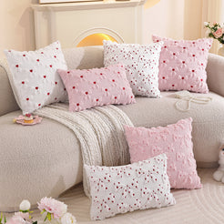 Embroidered woven polyester pillow covers with mixed pink bow and heart designs, arranged across a cream sofa
